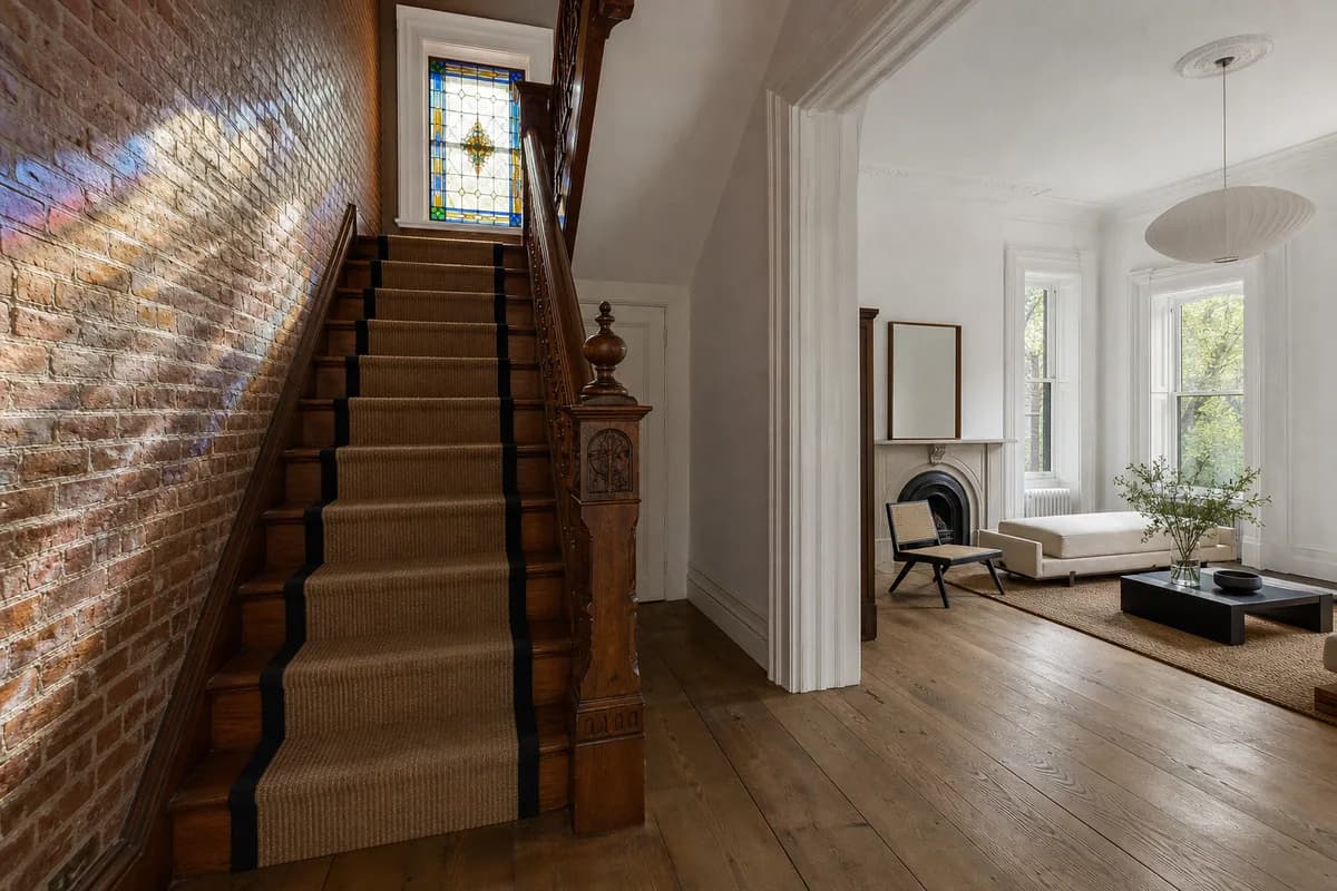 A restored Harlem townhouse stair hall with a carved newel post, exposed brick and a stained-glass transom