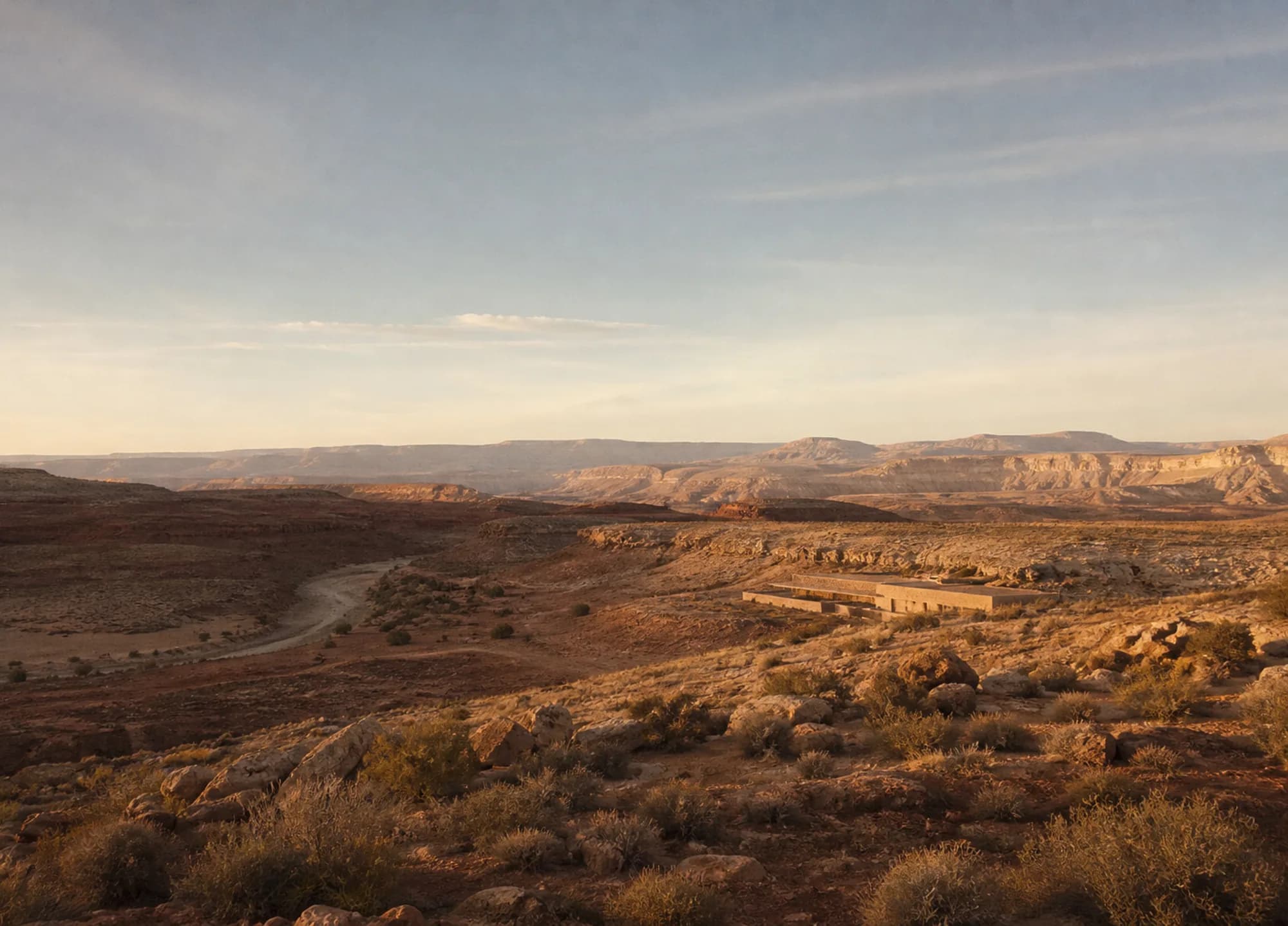 High desert at late afternoon, pale mesas layered to the horizon and a low resort building folded into the land