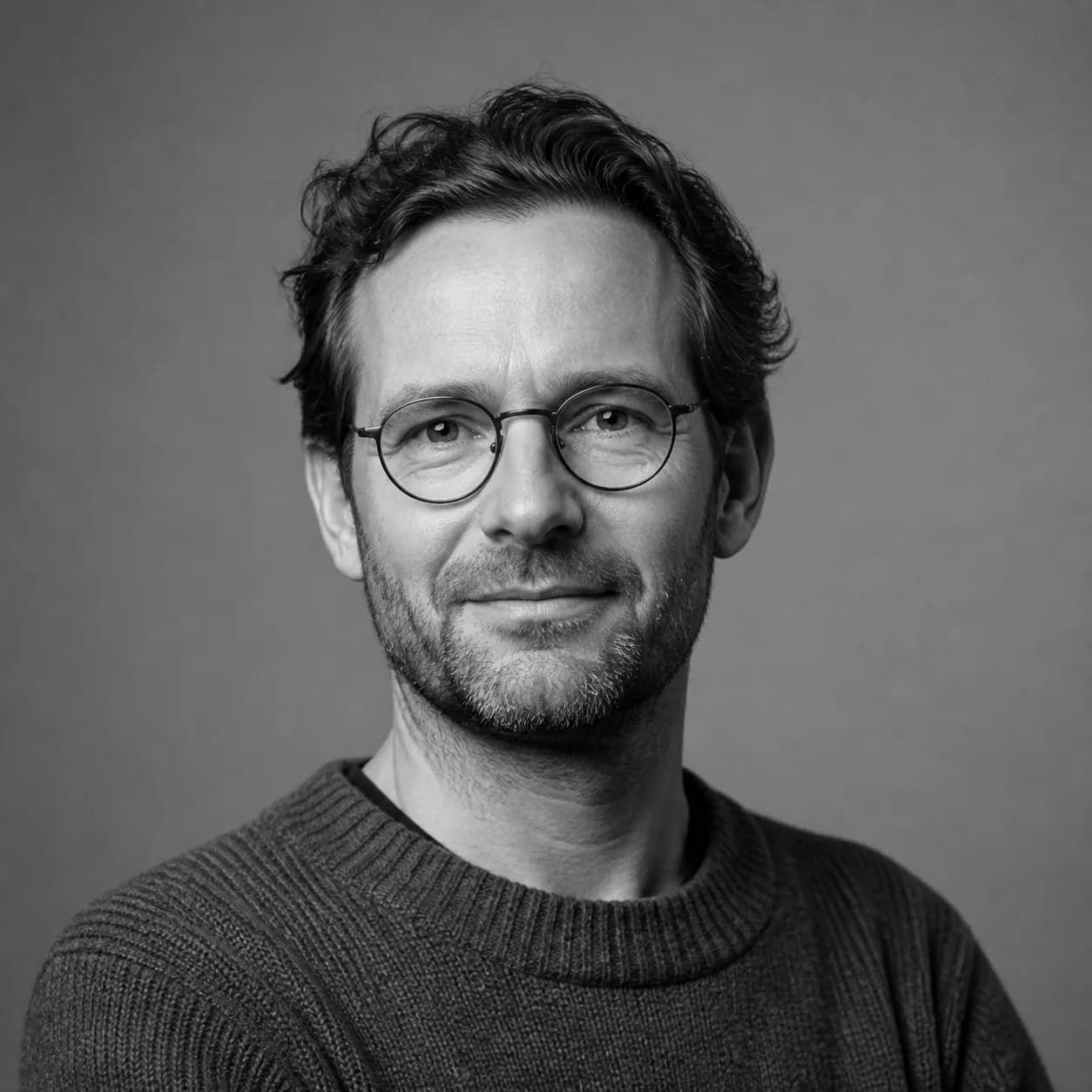 Black and white studio portrait of a presenter in round glasses