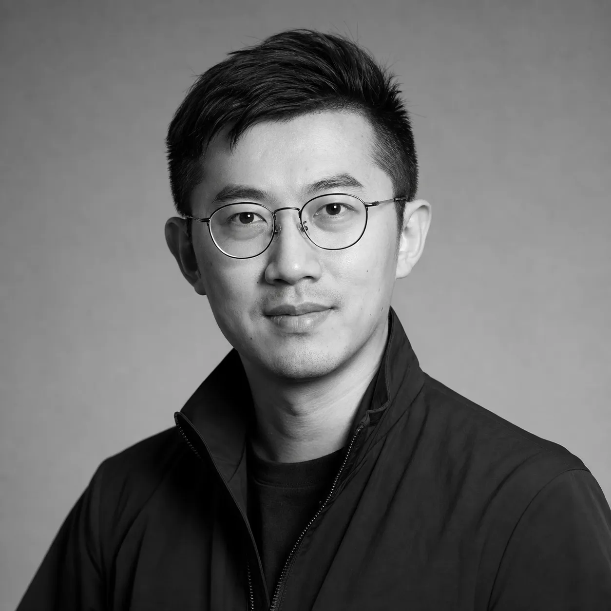 Black and white studio portrait of a presenter in wire glasses