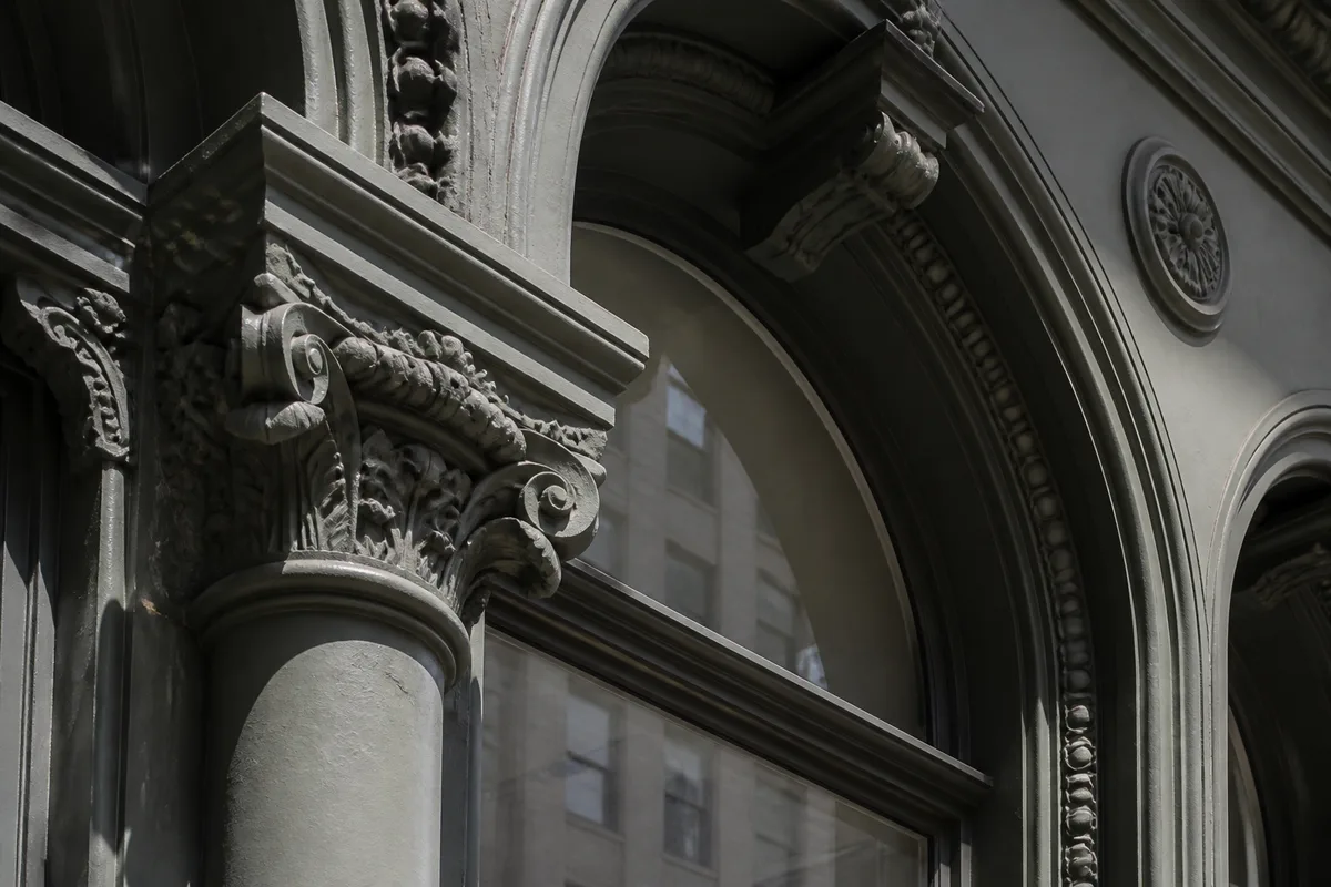A close view of a painted cast-iron column capital and the arched window head above it on a SoHo facade