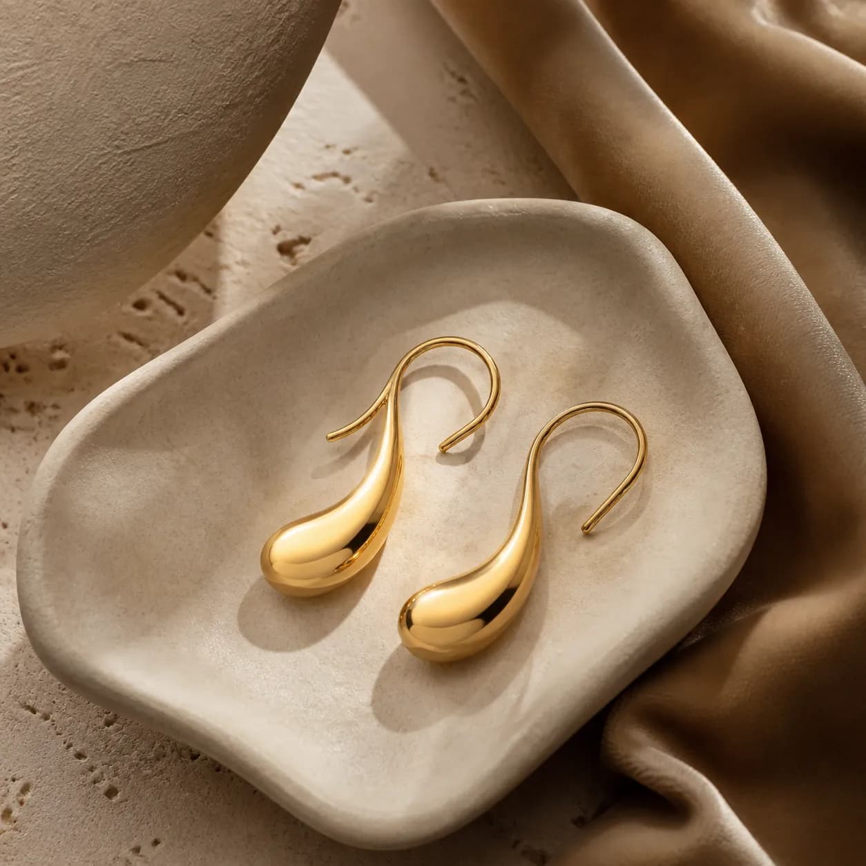A pair of fluid gold earrings resting in a shallow stone dish.