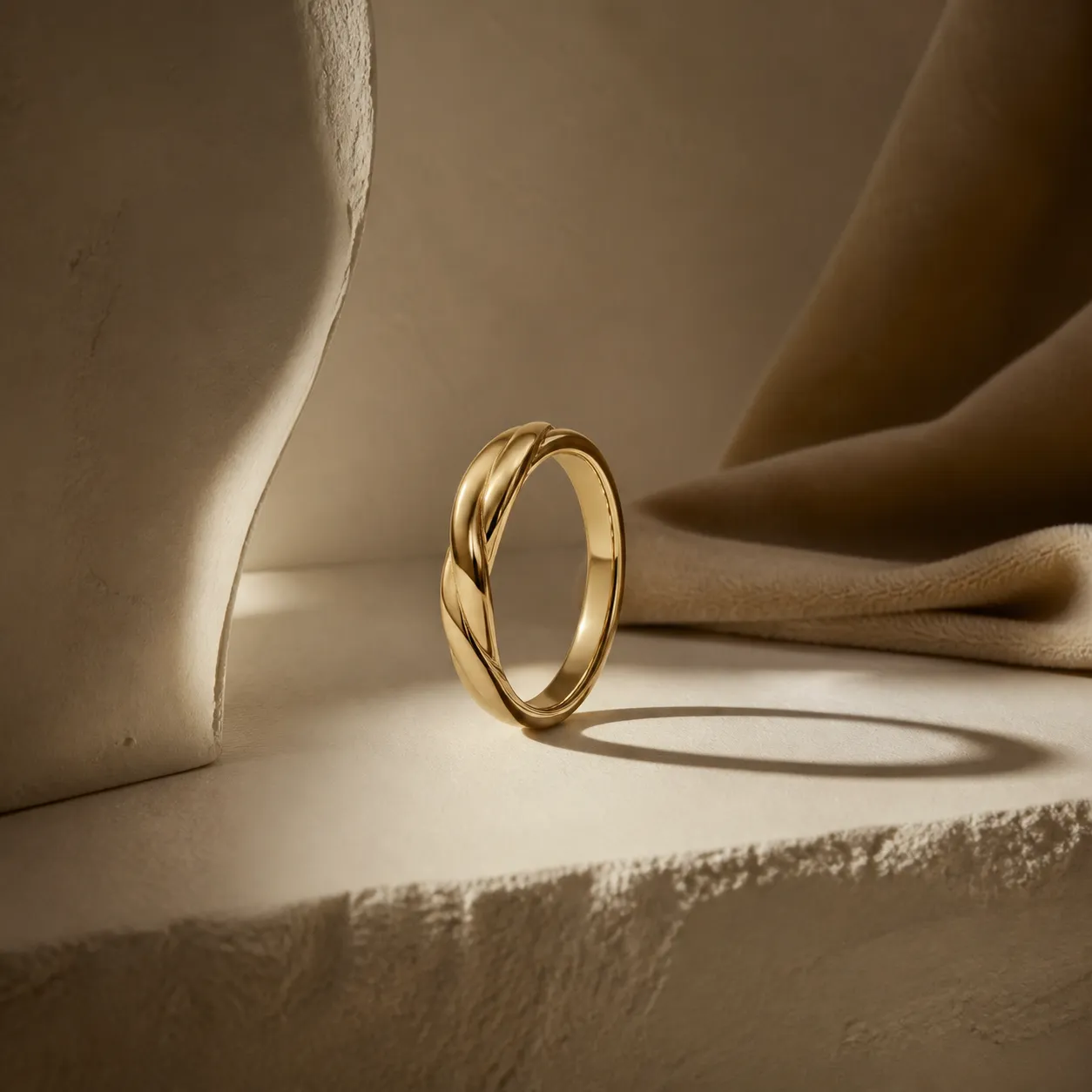A single twisted silver ring standing upright on matte plaster, casting a long soft shadow.