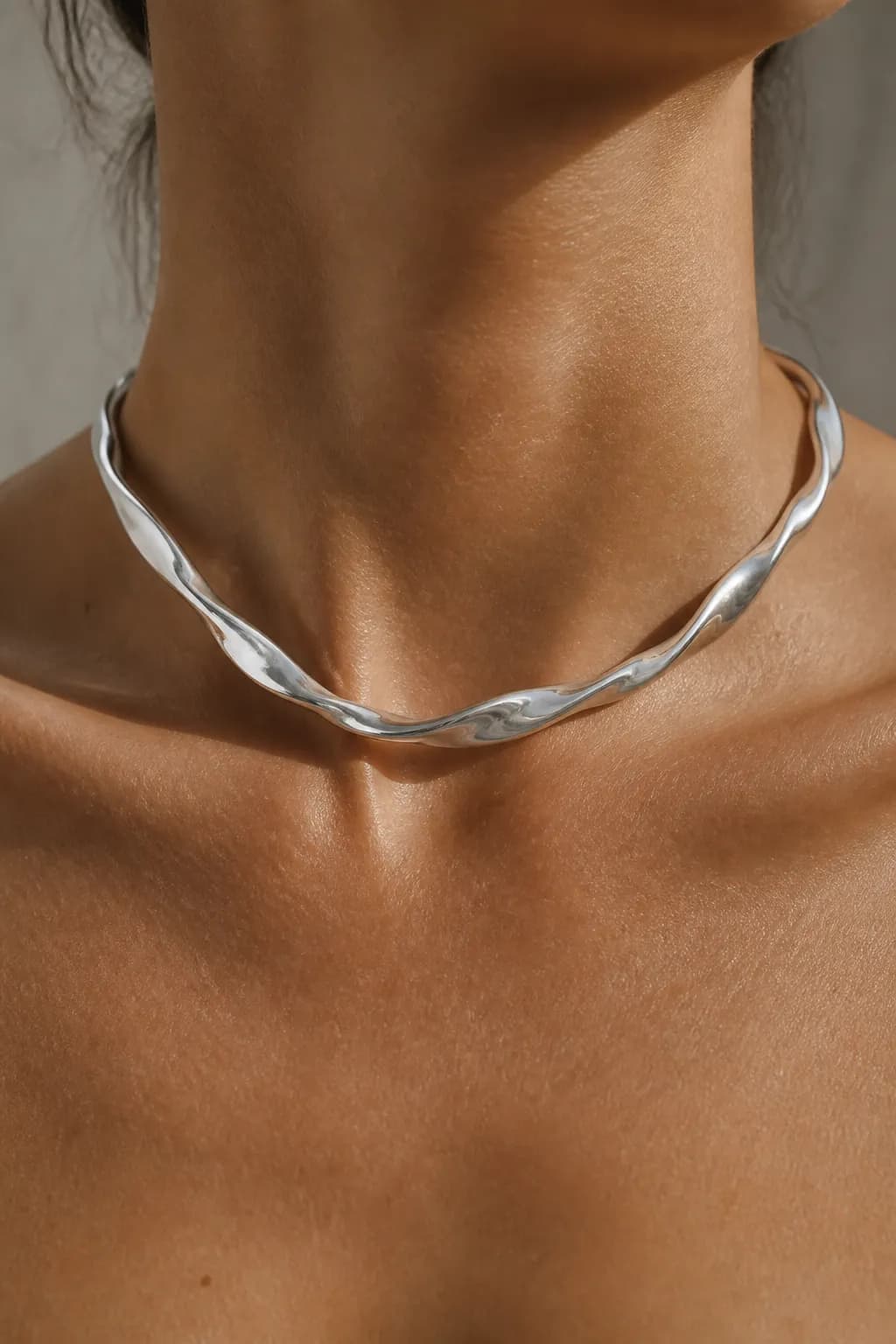 A collarbone and neck wearing a rigid twisted silver collar over bare skin, chin cropped out.