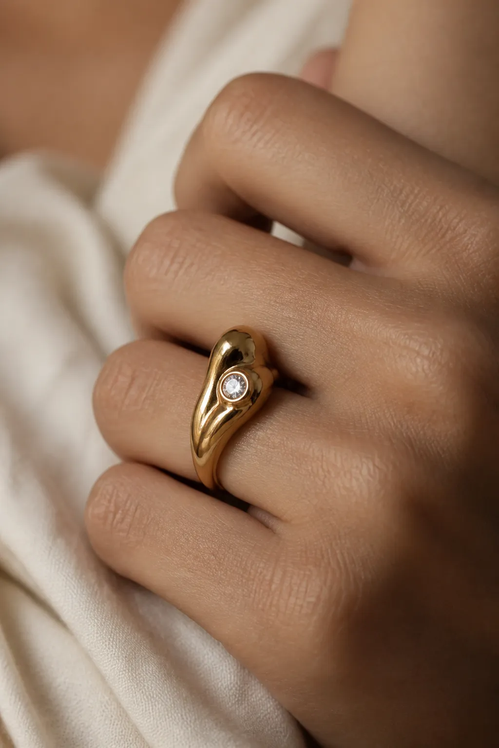 A gently closed fist showing one bold sculptural gold ring with a small white stone.