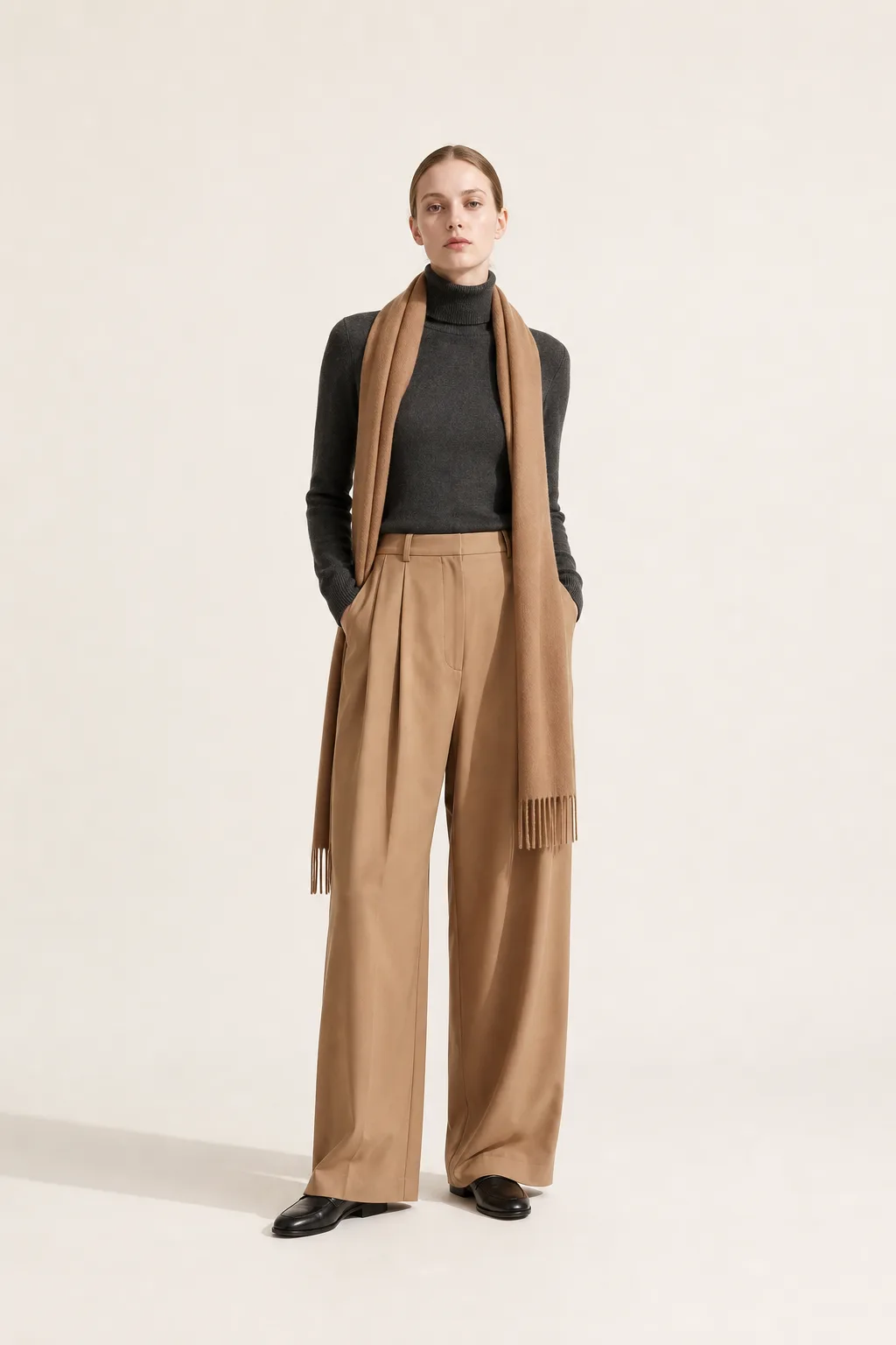 Full-length studio shot of a fine charcoal roll neck with a camel scarf draped long over wide camel trousers