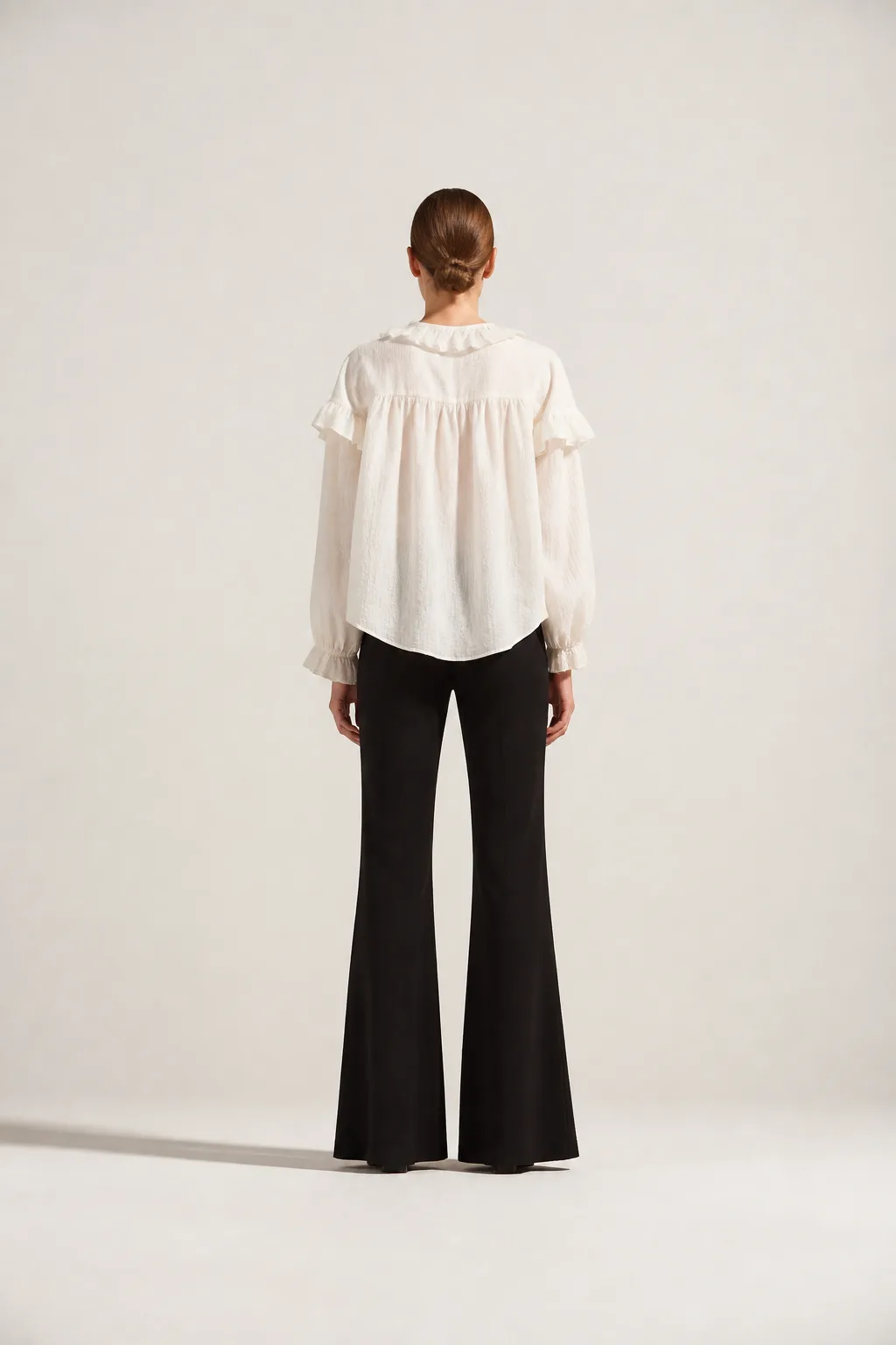Look 01 photographed from behind — the loose back drape of the blouse over floor-length flares